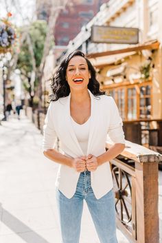 a woman in jeans and a white blazer smiling