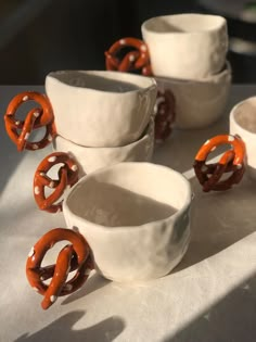 several white bowls with orange handles and rings on them are sitting on a tablecloth