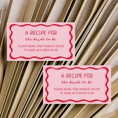 two pink business cards sitting next to each other on top of some sticks in front of a palm tree