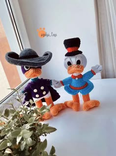 two crocheted ducks dressed in costumes, one wearing a hat and the other holding hands