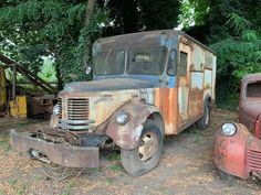 two old trucks are parked next to each other in the dirt near trees and bushes