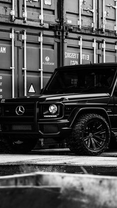 a black and white photo of a mercedes g - class parked in front of shipping containers