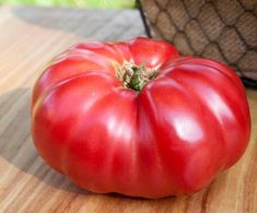 a red tomato sitting on top of a wooden cutting board