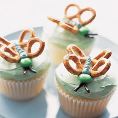 three cupcakes with green frosting and pretzels on top, sitting on a plate