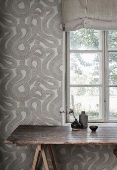 a wooden table sitting in front of a window next to a wallpapered wall