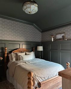 a large bed sitting under a ceiling light next to a wooden table and lamp shade