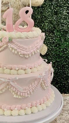 a pink and white tiered cake with candles in the shape of numbers on it