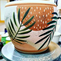 a pot with leaves painted on it sitting on a table next to other pots and bowls