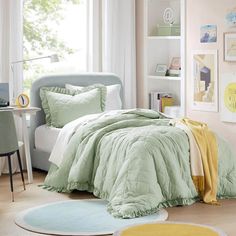 a bed with green comforter and pillows in a room next to a desk, chair and window