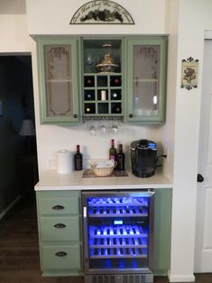 a kitchen with green cabinets and wine bottles on the shelves, along with a blue light under the cabinet