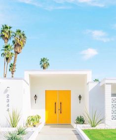 a yellow door is in front of a white house with palm trees and green grass