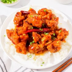 a white plate topped with chicken and rice next to chopsticks on a table