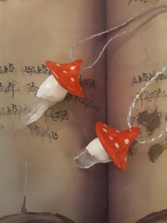 two red and white mushrooms are hanging from a book with writing on the pages behind them