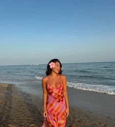 a woman standing on top of a sandy beach next to the ocean with a flower in her hair