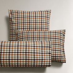 two pillows sitting next to each other on top of a white wall with brown and green plaid