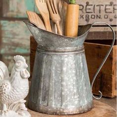 a metal bucket with utensils in it sitting on a table next to two chicken figurines