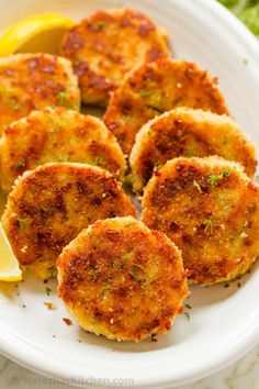 several crab cakes on a white plate with lemon wedges