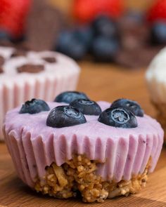 blueberries and granola on top of a wooden table next to cupcakes