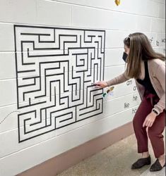 a woman wearing a face mask points at a maze on the wall