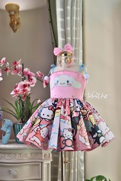 a dress with hello kitty on it sitting on top of a dresser next to flowers