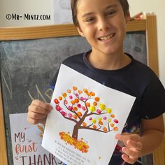 a young boy holding up a poster with an autumn tree on it