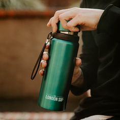 a person holding a green water bottle with the words london sip written on it while sitting down