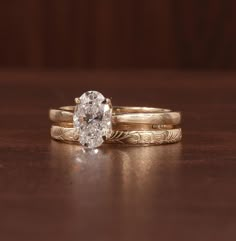 two gold wedding rings with an oval diamond in the center on a wooden table top