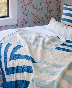 a bed with blue and white comforter next to a flowery wallpapered wall