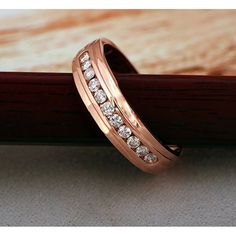 a rose gold wedding band with diamonds on it sitting on a wooden surface next to a piece of wood