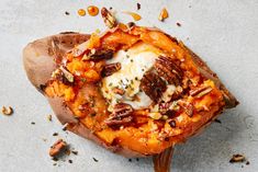 a baked sweet potato covered in nuts and cheese on a table with sauce drizzled over the top