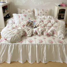 a white bed with pink flowers on it and a book laying on the pillowcase