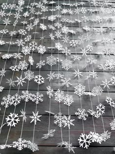 snowflakes are hanging from a wire on a wooden deck with string attached to it