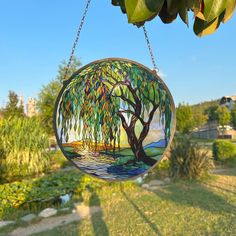 a stained glass hanging ornament with a tree and water scene in the background