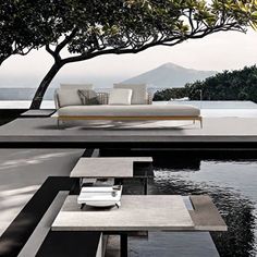 an outdoor living area with water, trees and couches by the pool in front of it