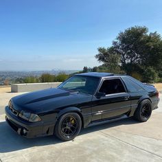 a black car parked on top of a cement parking lot next to trees and bushes