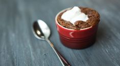 a red cup filled with pudding and whipped cream on top of a wooden table next to a spoon