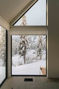 the inside of a house with large windows and snow covered trees in the back ground