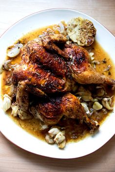 a white plate topped with chicken covered in gravy and potatoes on top of a wooden table