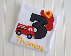 a birthday shirt with a firetruck and hat on it's front, the number three is for thomas