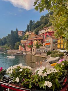 an image of a town on the shore with flowers around it and boats in the water