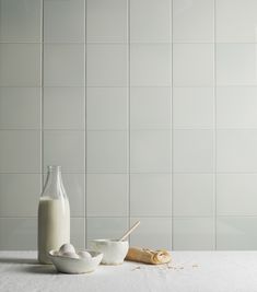 a bottle of milk next to two bowls and a spoon on a white counter top