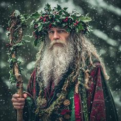 an old man with a long beard and wreath on his head holding a stick in the snow