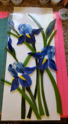 some blue flowers are sitting on a piece of paper next to paint cans and scissors