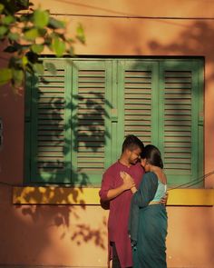 a man and woman standing in front of a window with shutters on each side