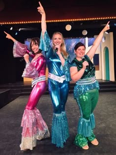 three women in sequins posing for a photo on stage with their arms up