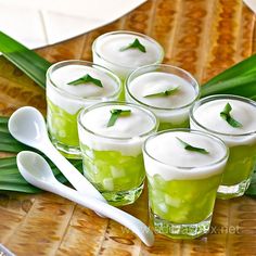 several glasses filled with green liquid sitting on top of a table next to spoons