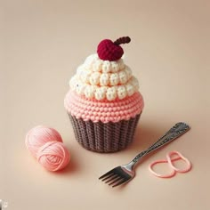 a crocheted cupcake with a cherry on top next to yarn and scissors