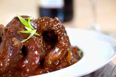 a white plate topped with meat covered in sauce and garnished with green leaves