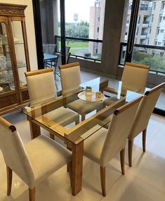 a glass dining table with beige chairs in front of a large window overlooking the city