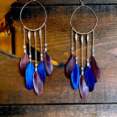 two pairs of earrings with chains hanging from them on a wooden table next to a plant